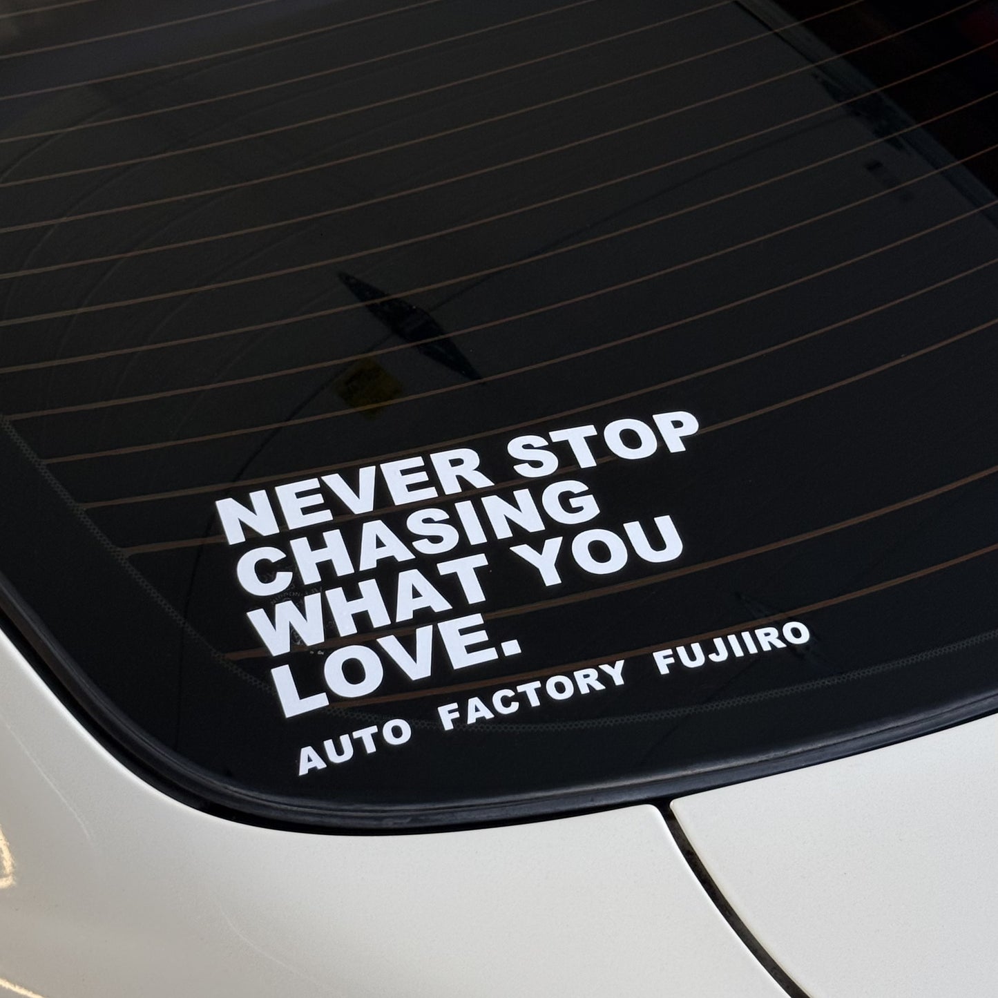 NEVER STOP CHASING WHAT YOU LOVE decal on the rear glass of a white Nissan