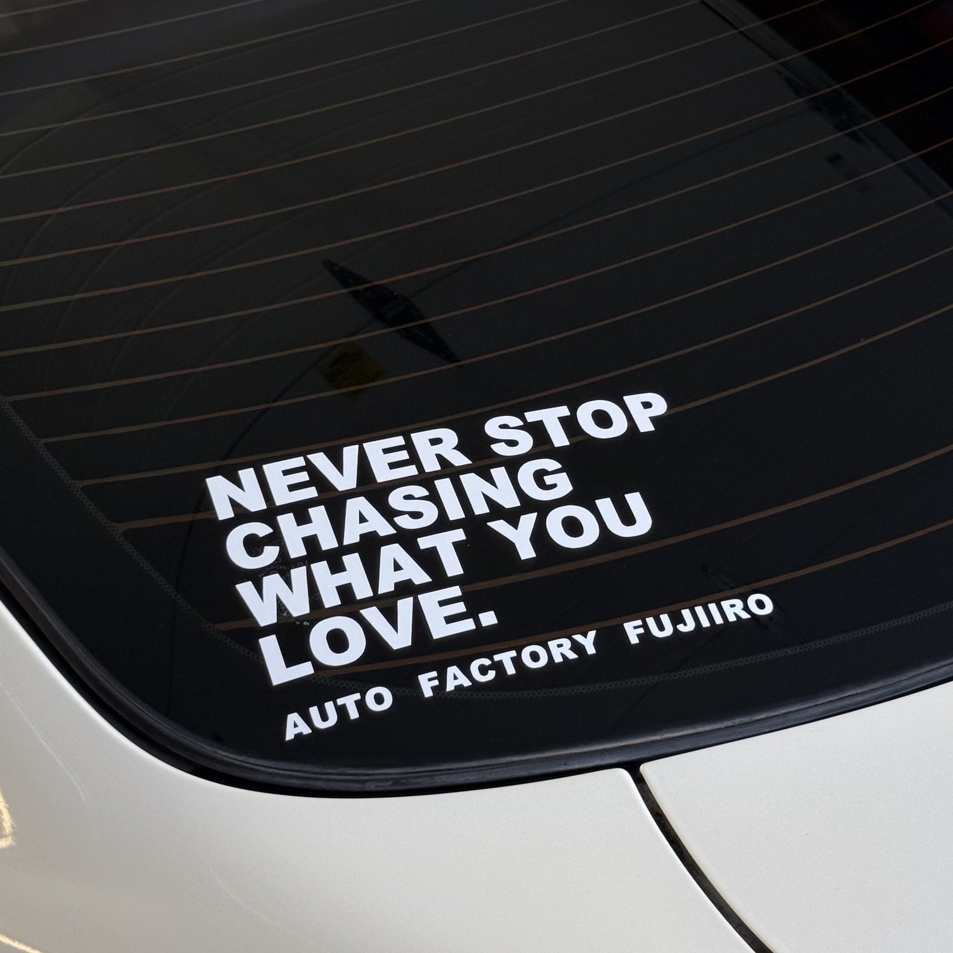 NEVER STOP CHASING WHAT YOU LOVE decal on the rear glass of a white Nissan