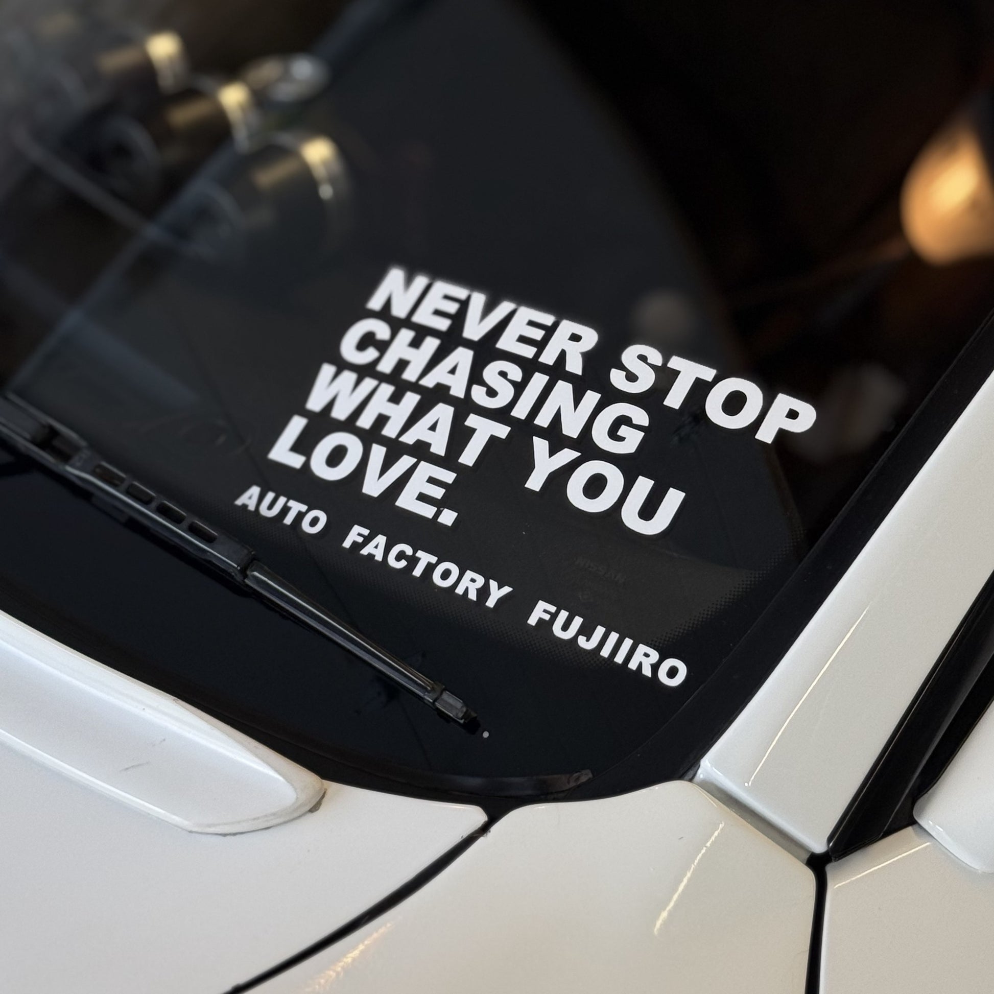 NEVER STOP CHASING WHAT YOU LOVE decal applied to the windshield of a white Nissan