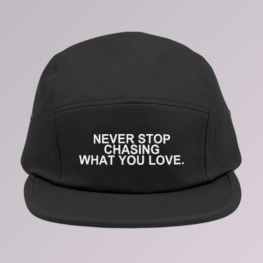 Black — NEVER STOP CHASING WHAT YOU LOVE five-panel cap, front view, slogan embroidered across the front panel